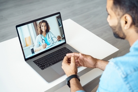 View over patient shoulder sitting at desk receiving online medical consultation.